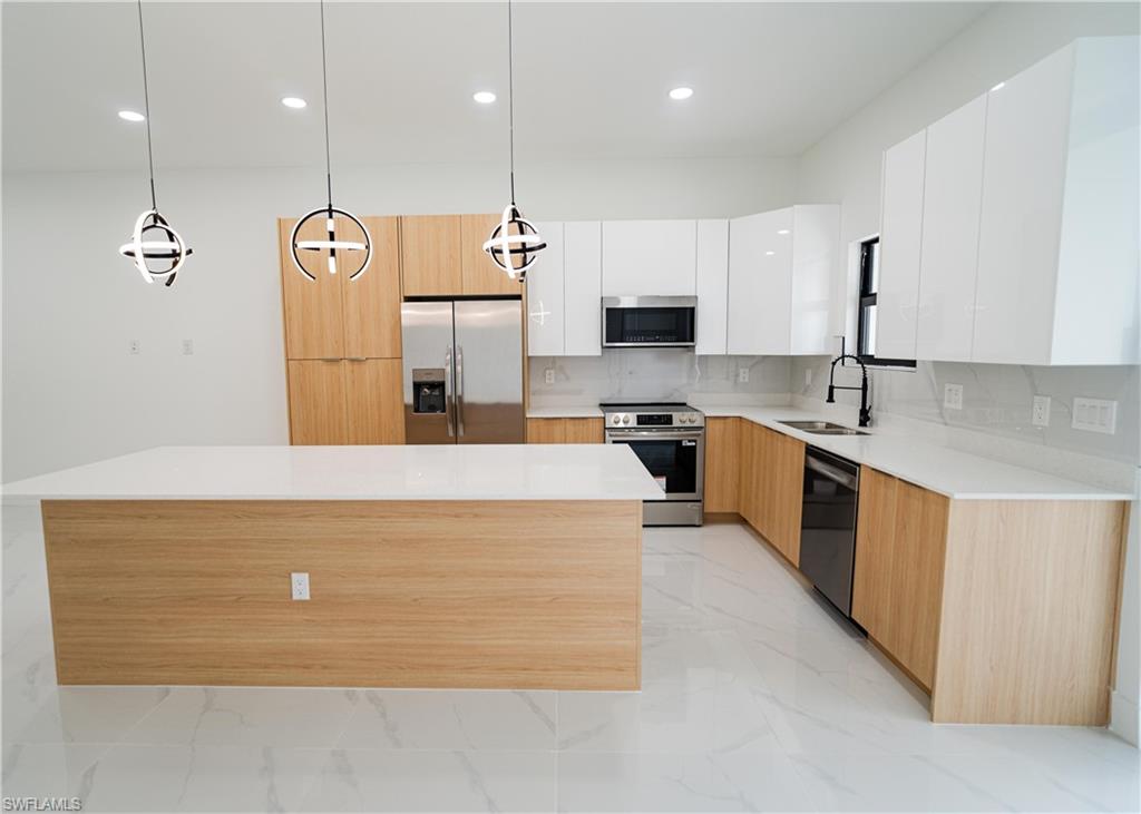 Contemporary kitchen featuring a large center island with a white countertop, two-tone cabinetry with wood-finish lower cabinets and white upper cabinets, stainless steel appliances, and matching white countertops with a light-colored backsplash
