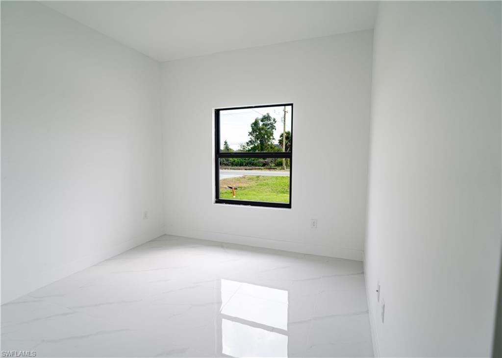 Bright interior space featuring a window with black trim, white walls, and polished white tile flooring with subtle veining