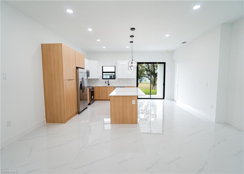 Open-concept kitchen featuring wood-tone and white cabinetry, a central island with a white countertop, stainless steel appliances, and a modern pendant light fixture