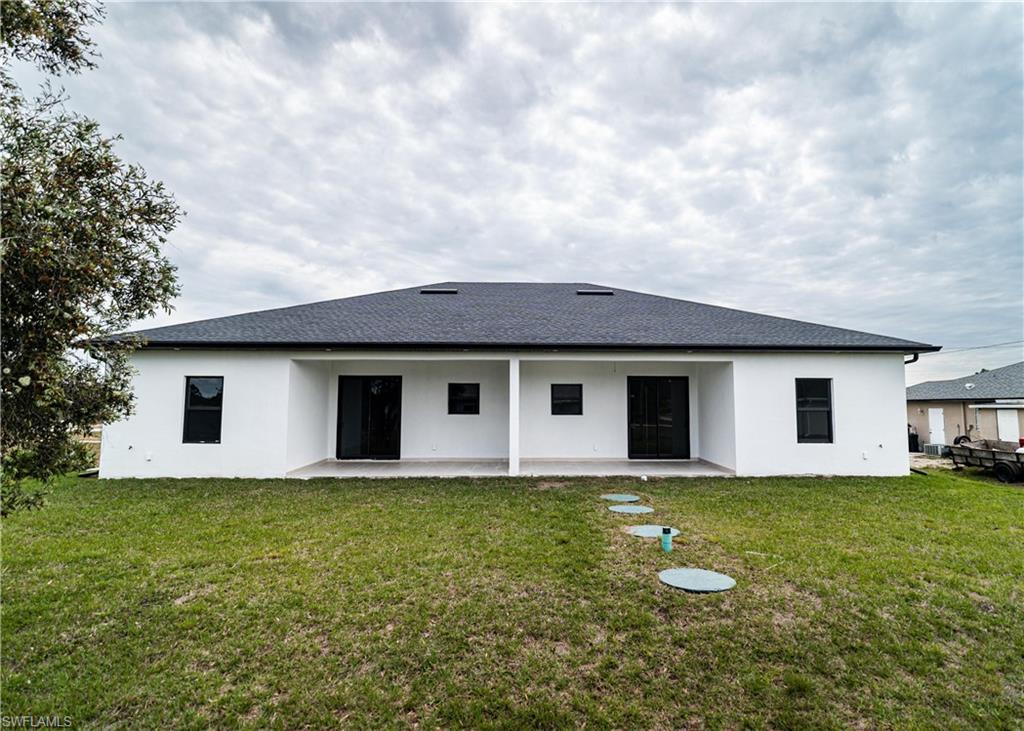 Rear exterior featuring a white stucco finish and a dark shingle roof