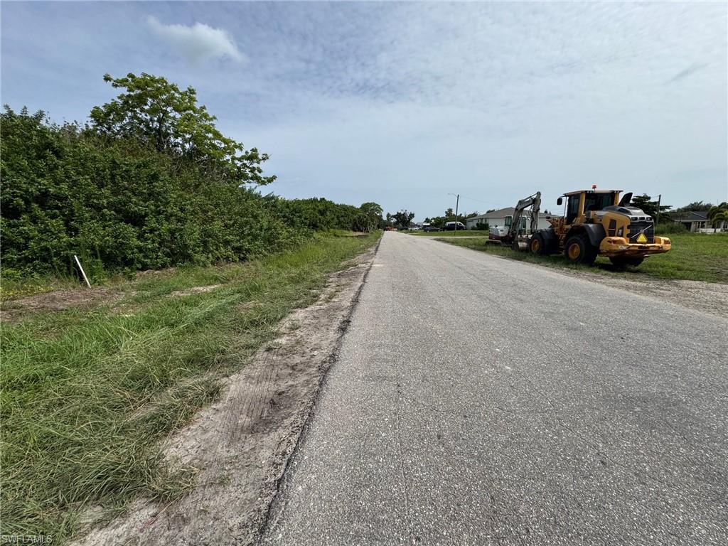 Roadside property featuring a paved road, undeveloped land with natural vegetation, and distant residential structures