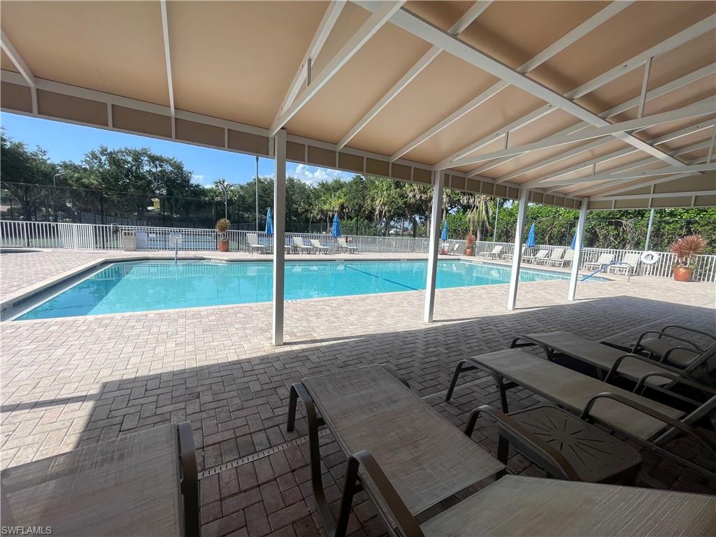 Expansive outdoor pool area featuring a rectangular swimming pool, herringbone brick paver decking, and a shaded pergola structure