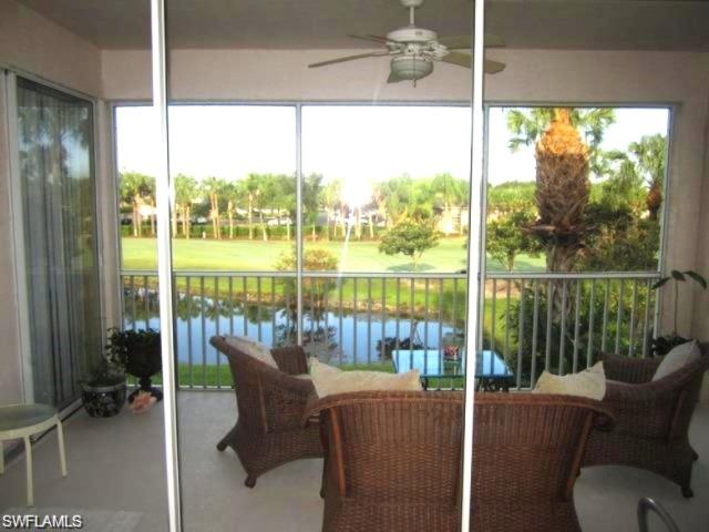 Screened balcony featuring a ceiling fan, sliding glass door access, and a water-frontage view overlooking a golf course with mature palm trees.