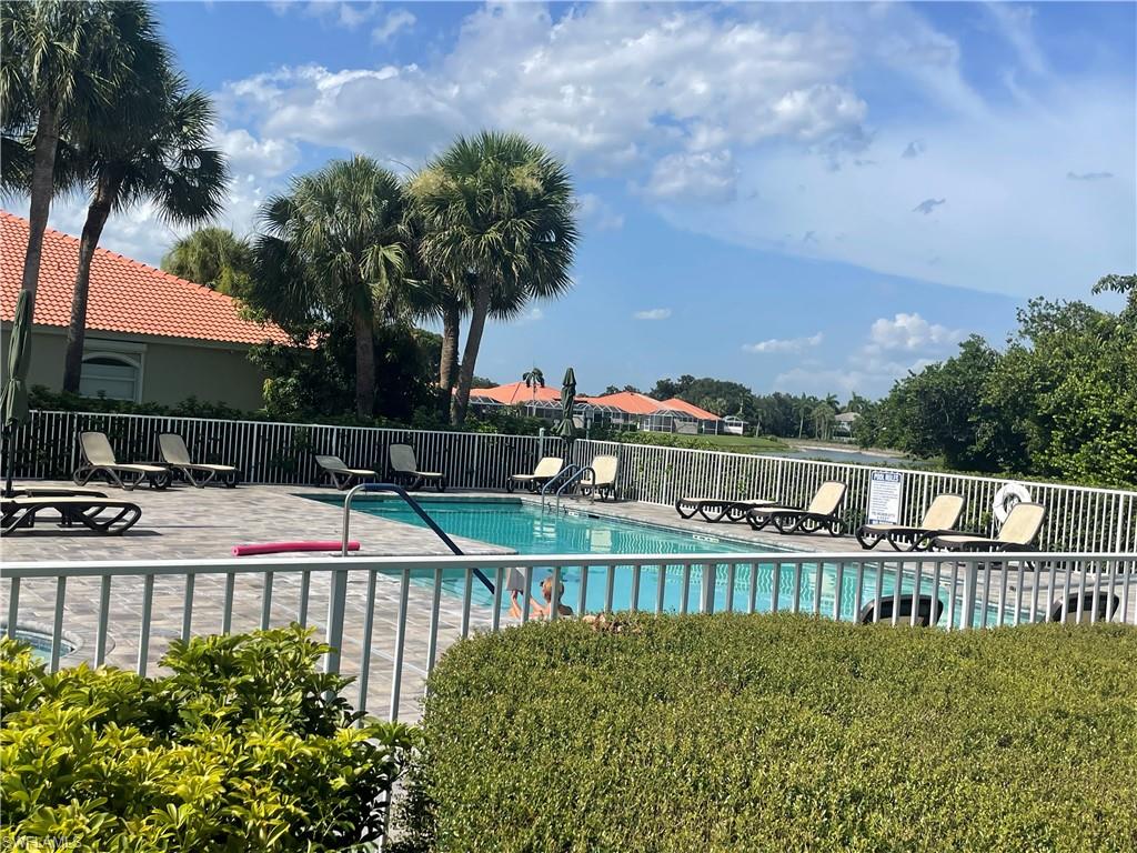 Subdivision community  pool with a surrounding white fence, paver patio, and mature tropical landscaping.