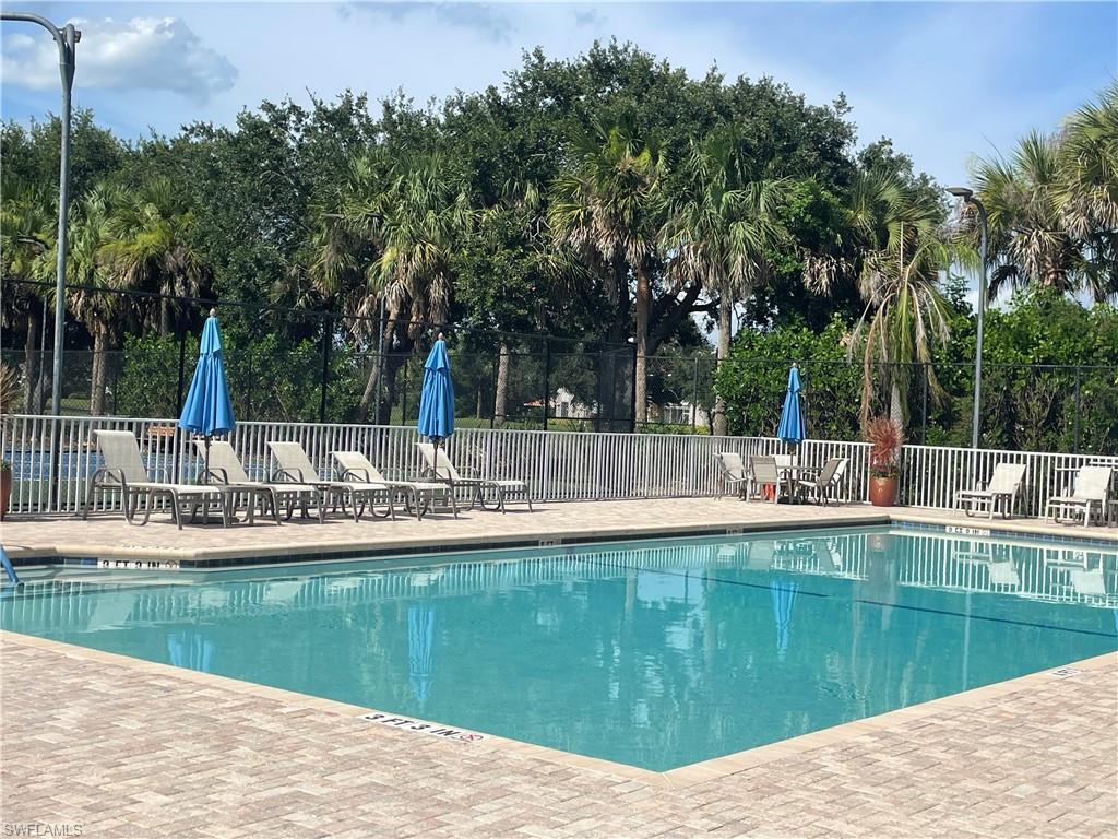 Outdoor swimming pool featuring a paver deck, white perimeter fencing, and mature tropical landscaping