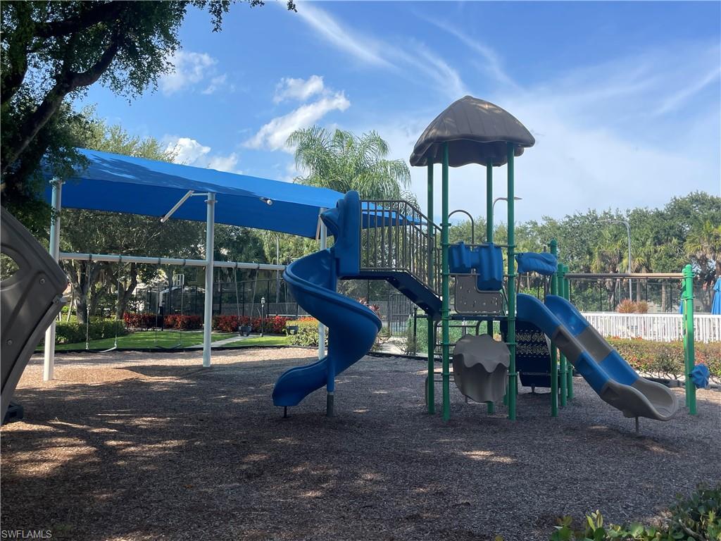 Playground area featuring a multi-level play structure with multiple slides, a thatched roof, and a blue shade canopy