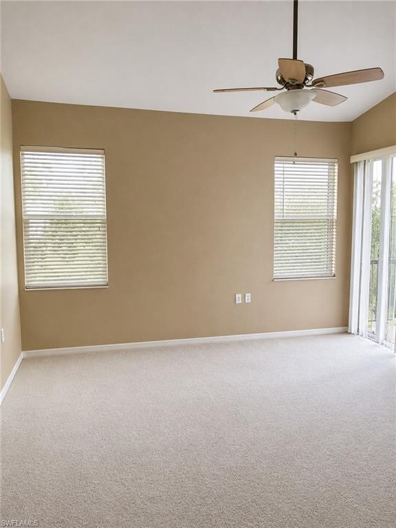 Spacious room featuring neutral carpeting, a ceiling fan with integrated lighting, two windows with blinds, and a sliding glass door