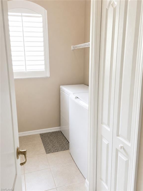 Dedicated laundry area featuring ceramic tile flooring, a built-in wire shelf, and an arched window with plantation shutters