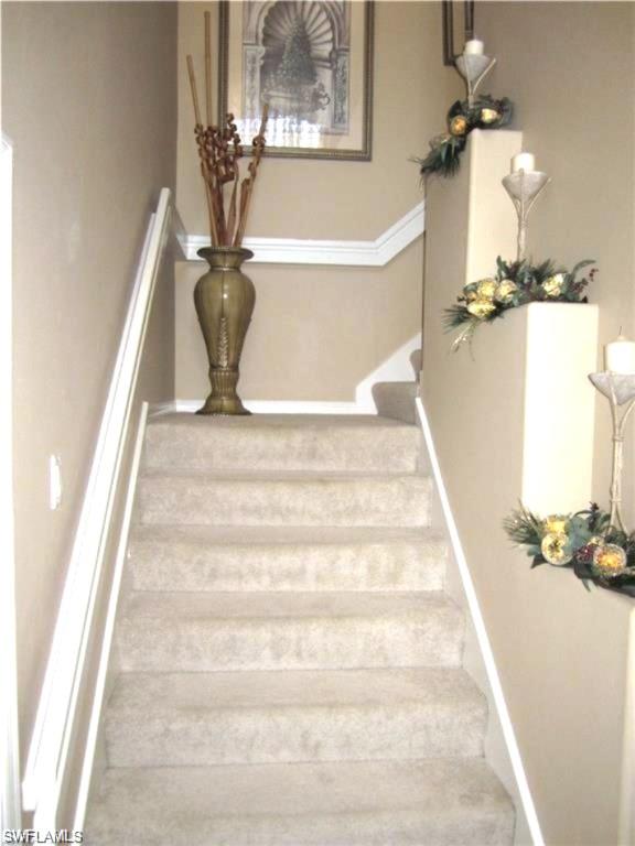 Carpeted staircase featuring a white handrail and crown molding details