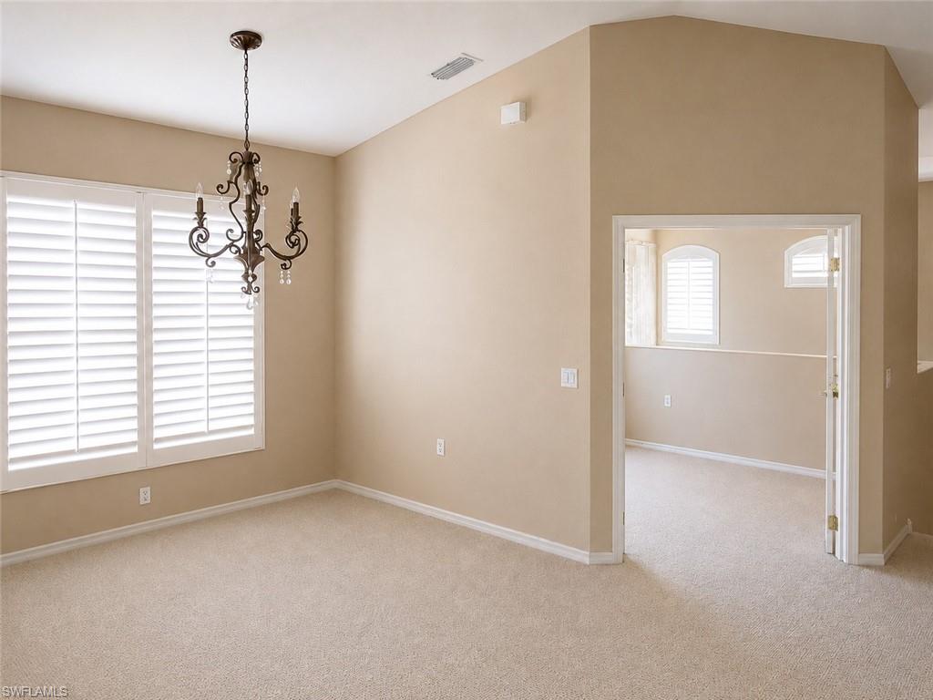 Room with vaulted ceiling, featuring a decorative chandelier and neutral-toned carpet flooring