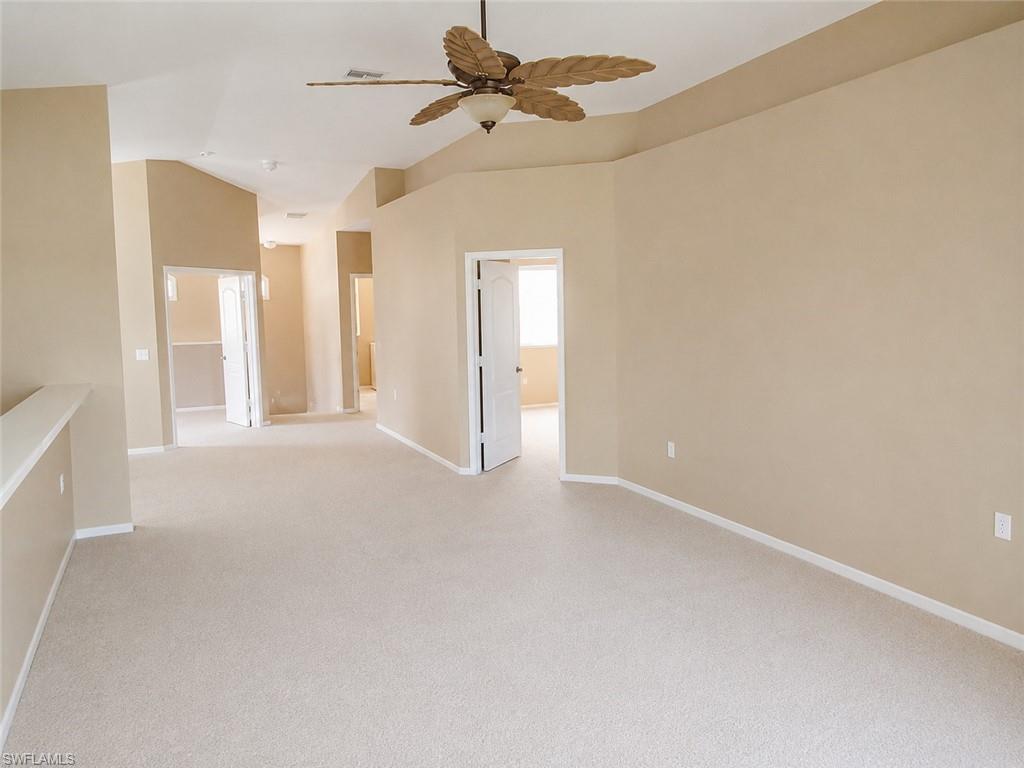 Spacious living room with neutral-toned carpeting and walls, featuring a decorative ceiling fan.