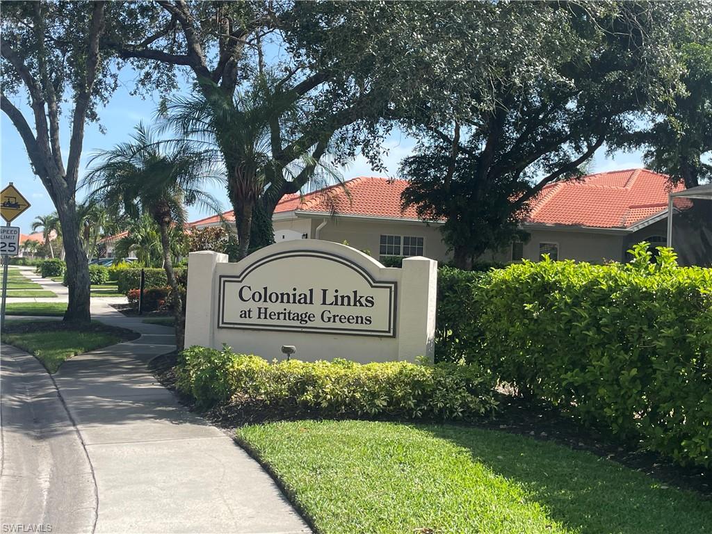 Entry monument for Colonial Links at Heritage Greens, featuring manicured landscaping, mature trees, and visible red tile roofs of residences.