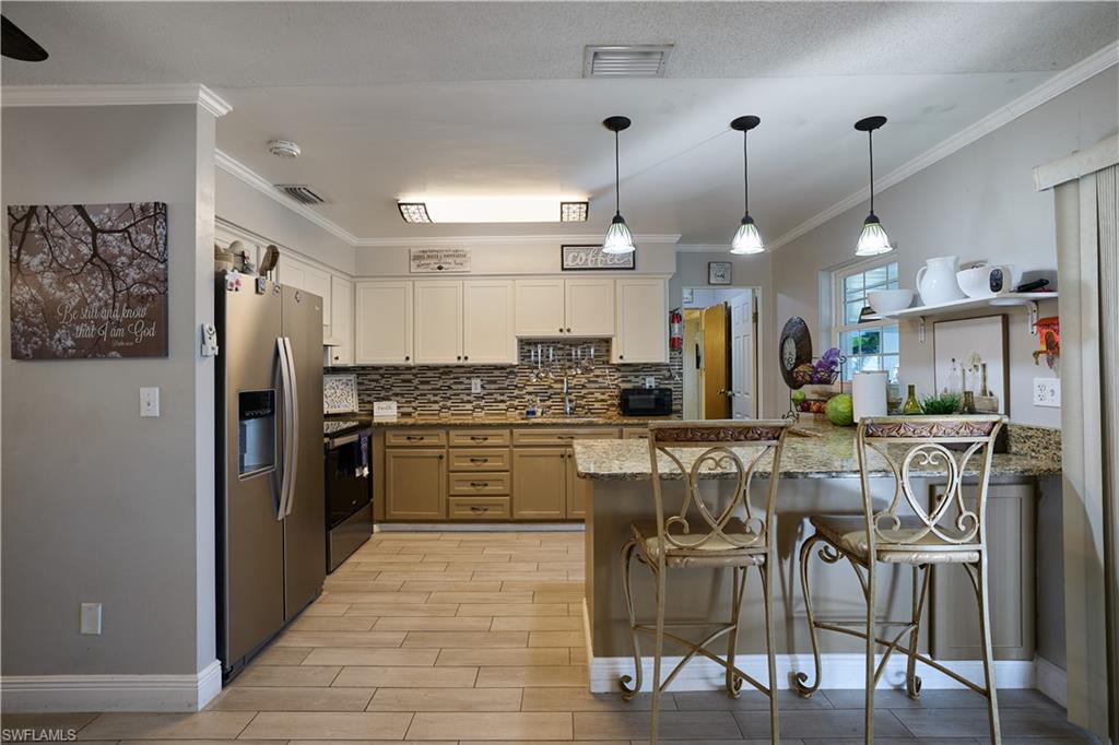 Open-concept kitchen featuring wood-finish tile flooring, a multi-tone tile backsplash, and a granite countertop island with pendant lighting