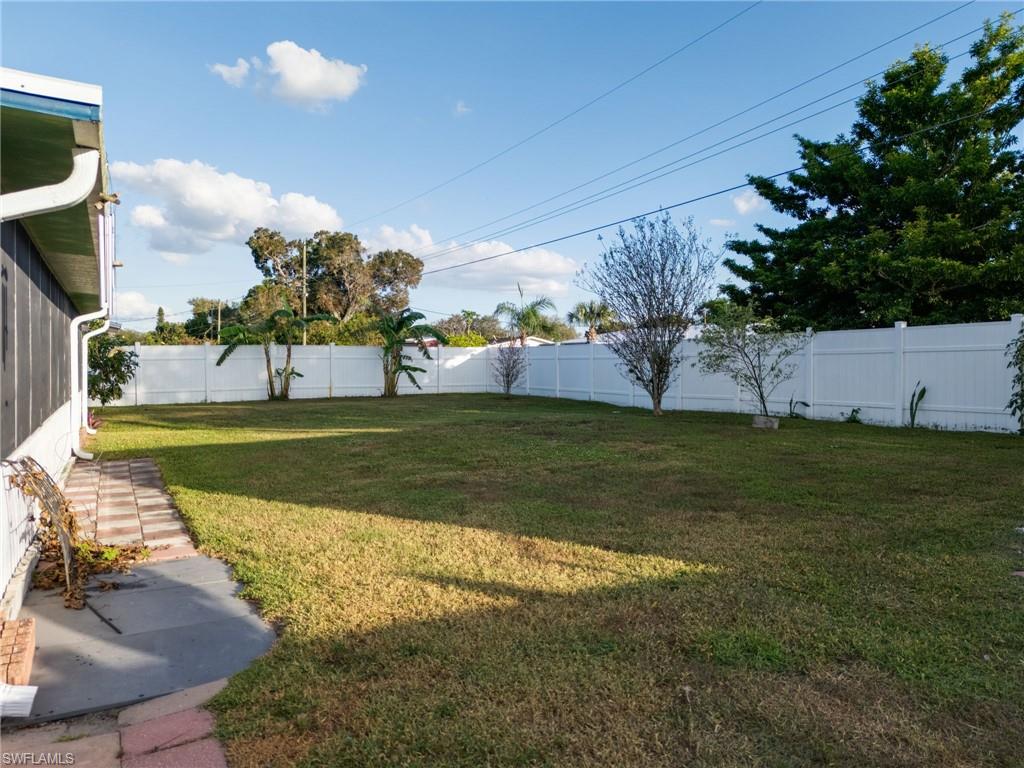Expansive backyard featuring a green lawn, full white privacy fencing, and mature trees