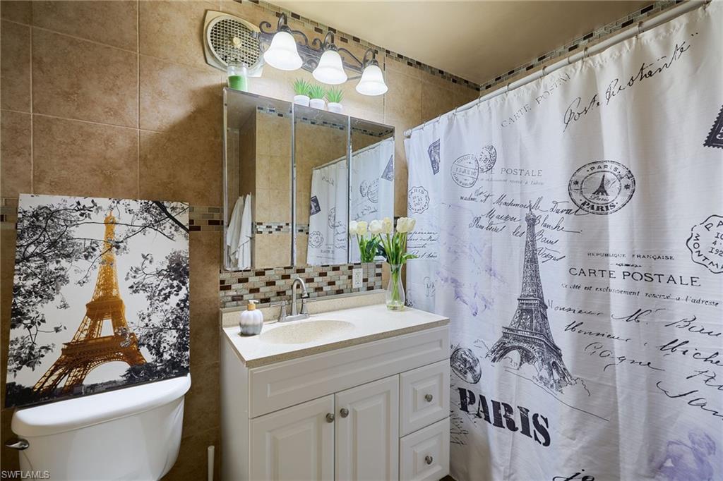 Bathroom featuring a white vanity with an integrated sink, tri-fold mirrored medicine cabinet, and sconce lighting