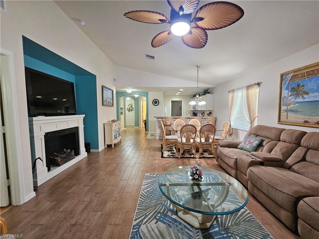 Spacious open-concept living area featuring wood-finish flooring, a vaulted ceiling, and a fireplace with a white mantel