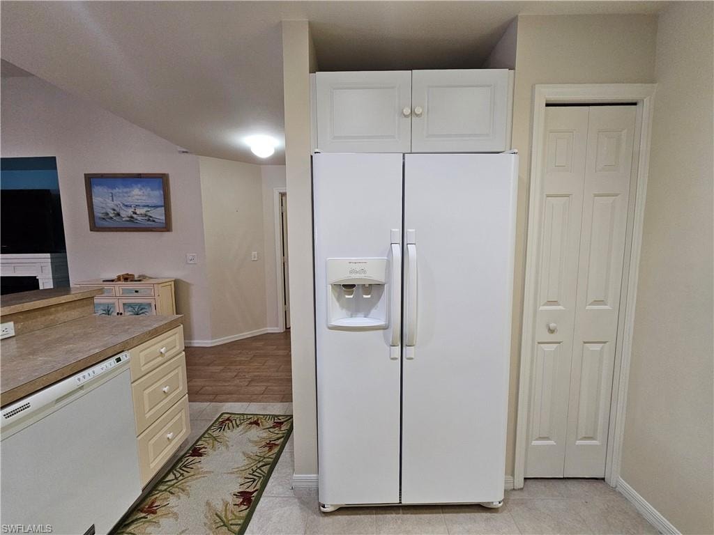 Kitchen area featuring a side-by-side refrigerator, upper white cabinetry, light-toned countertops, and tile flooring