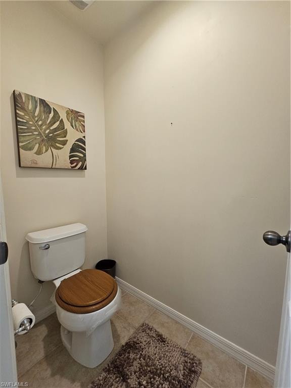 Bathroom featuring a toilet with a wood-finish seat and ceramic tile flooring