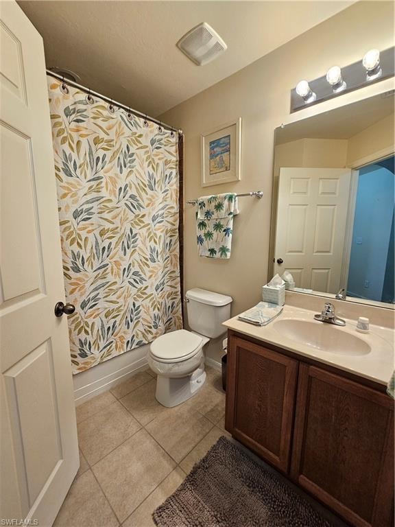 Bathroom featuring a white toilet, tile flooring, a shower/tub combination, a vanity with wood-finish cabinetry, and a countertop with an integrated sink