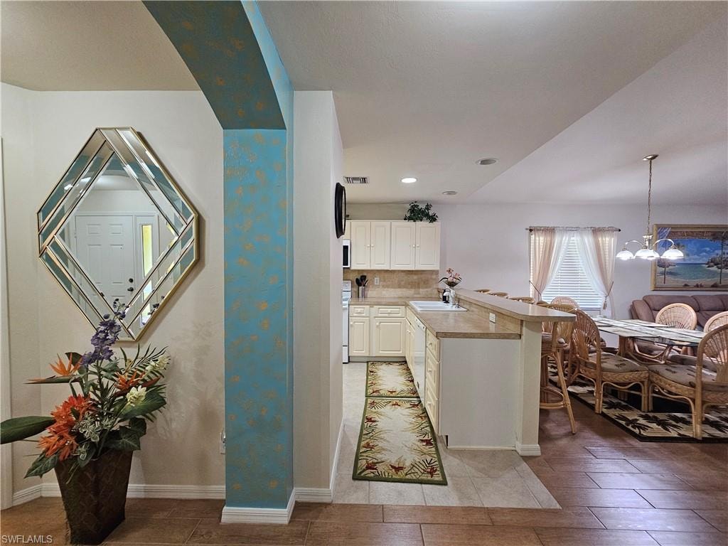 Open-concept living space featuring a kitchen with light cabinetry and a breakfast bar, a dining area with a chandelier, and a living area with a large window