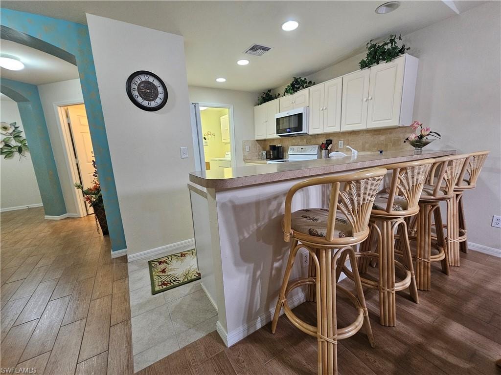Kitchen with light-toned cabinetry, a built-in microwave, and a breakfast bar
