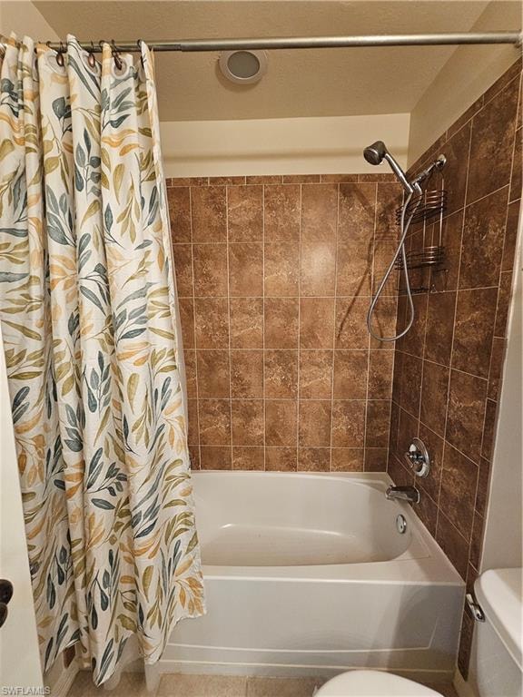 Bathtub and shower combination featuring brown square wall tiles, a ceiling-mounted exhaust fan, and chrome fixtures