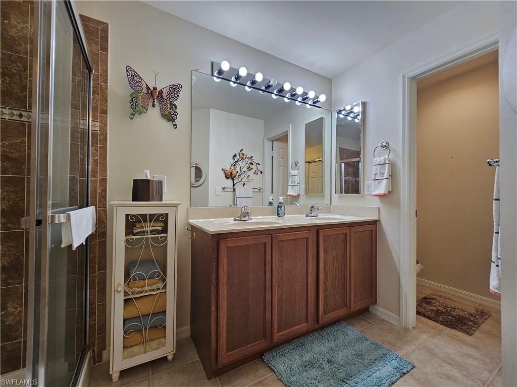 Bathroom featuring a double vanity with wood-finish cabinetry, a large mirror with integrated lighting, and a glass-enclosed shower with tiled walls