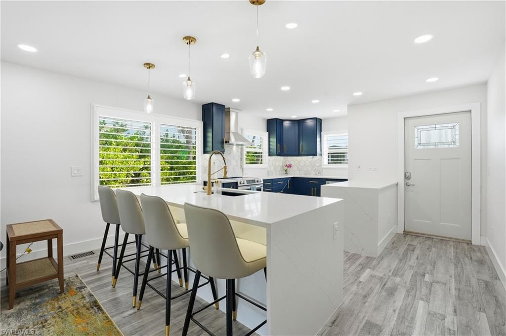 Kitchen featuring a peninsula, blue cabinetry, a breakfast bar, light stone countertops, and hanging light fixtures - Virtually Edited Image