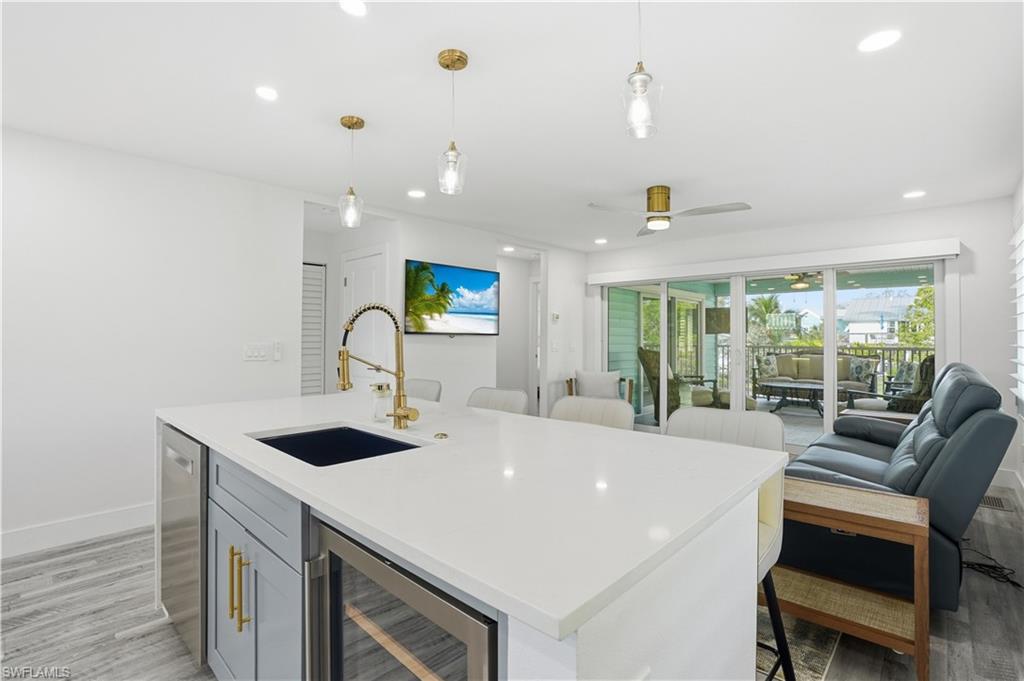 Kitchen with light wood finished floors, beverage cooler, hanging light fixtures, open floor plan, and light stone countertops - Virtually Edited Image