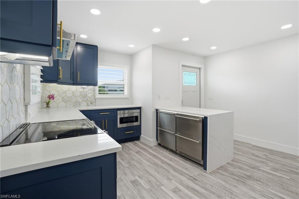 Kitchen with a peninsula, light stone countertops, blue cabinets, recessed lighting, and tasteful backsplash - Virtually Edited Image