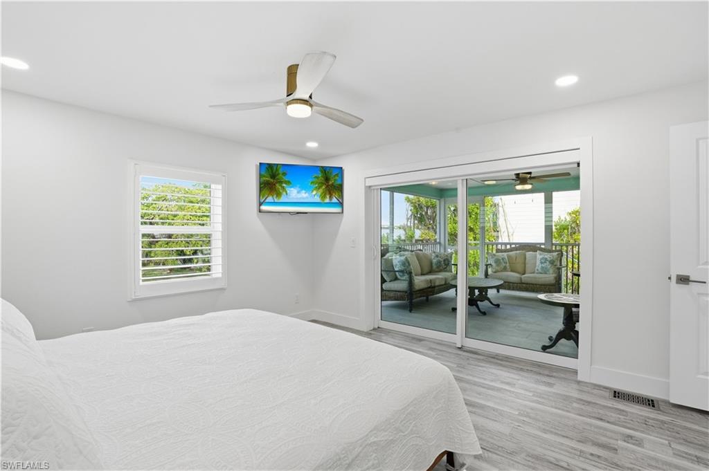 Bedroom with light wood finished floors, multiple windows, ceiling fan, recessed lighting, and access to exterior - Virtually Edited Image