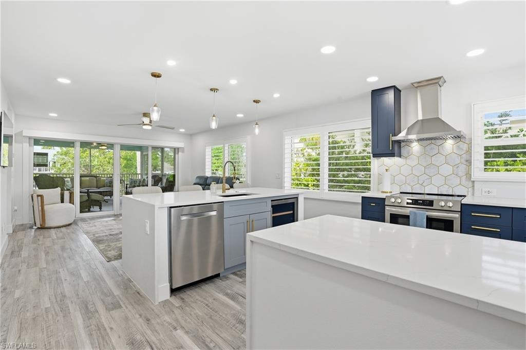 Kitchen with ceiling fan, light stone counters, decorative light fixtures, stainless steel appliances, and a center island with sink - Virtually Edited Image