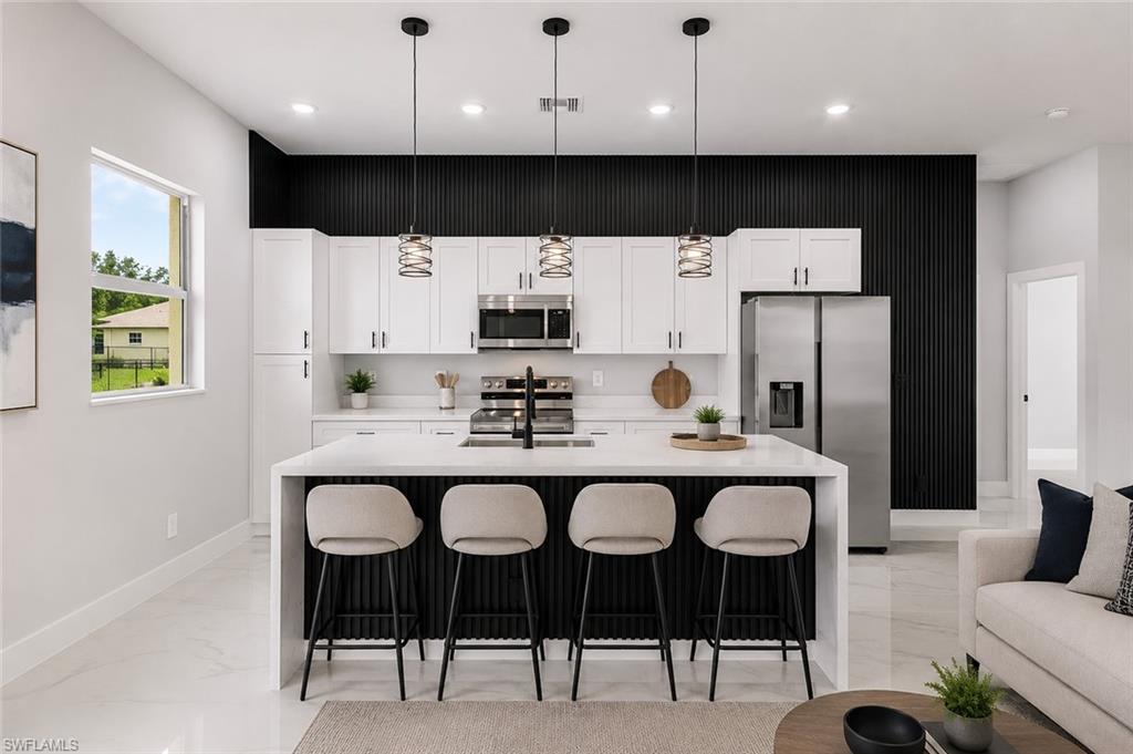 Modern kitchen featuring a waterfall island, white cabinetry, stainless steel appliances, and a black accent wall