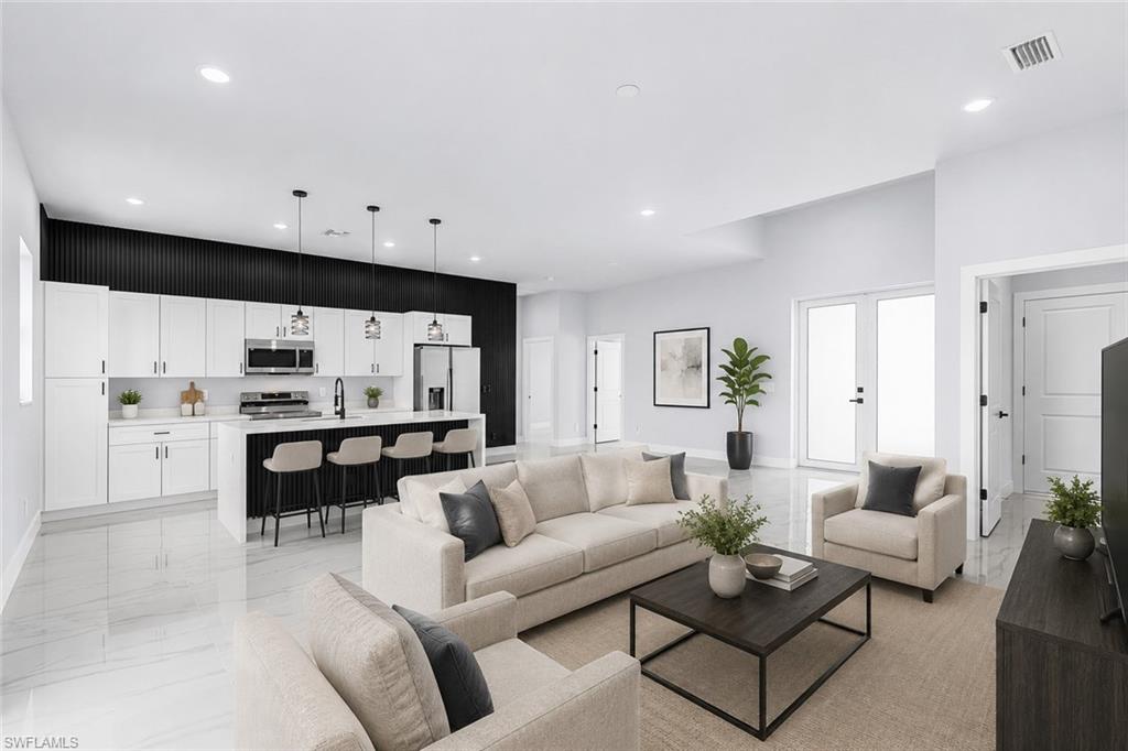 Contemporary open-concept living space with a kitchen featuring white cabinetry, stainless steel appliances, a center island with pendant lighting, and a black accent wall