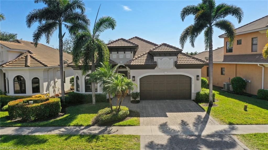 Mediterranean-style residence featuring a tile roof, stucco exterior, arched garage door, paver driveway, and mature palm trees
