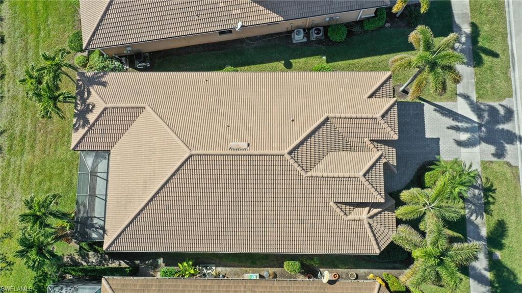 Tile roof with multiple gables, screened enclosure, mature palm trees, paved driveway, and manicured landscaping