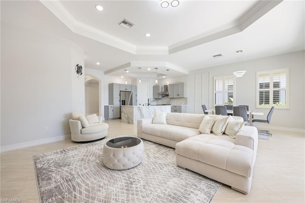 Open-concept living space featuring a tray ceiling with recessed lighting, light-toned tile flooring, and plantation shutters
