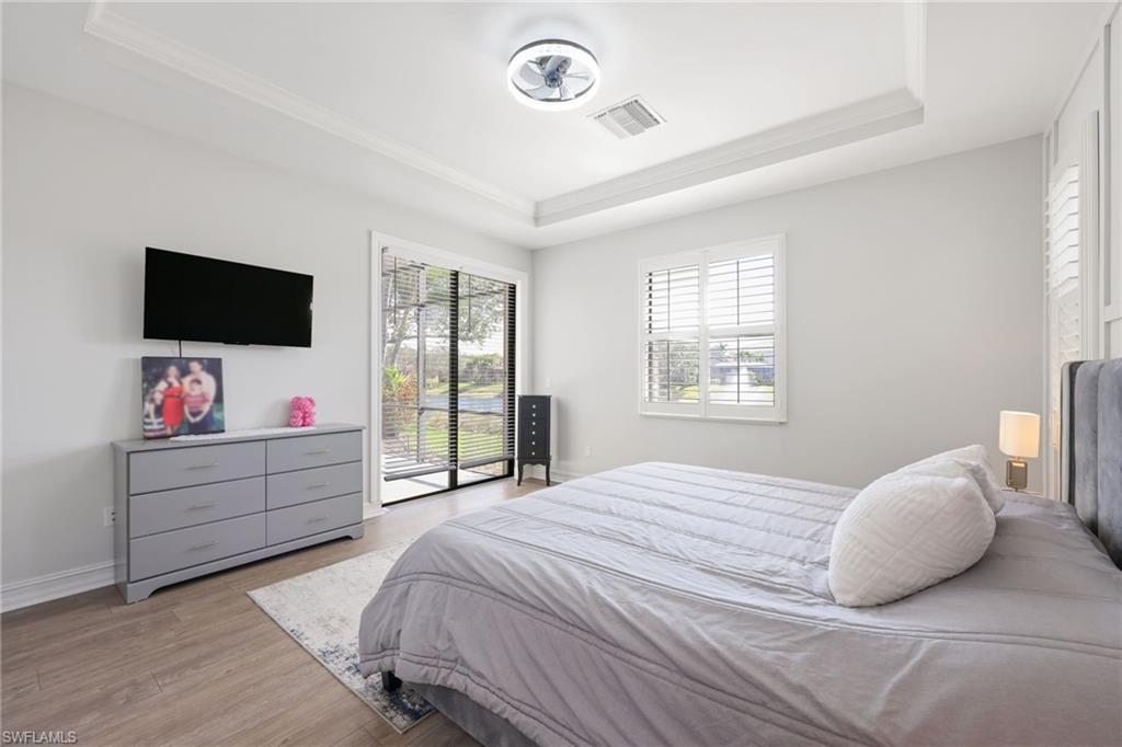Recessed ceiling with crown molding, wood-finish flooring, sliding glass door, white plantation shutters, and a modern ceiling fan with integrated lighting