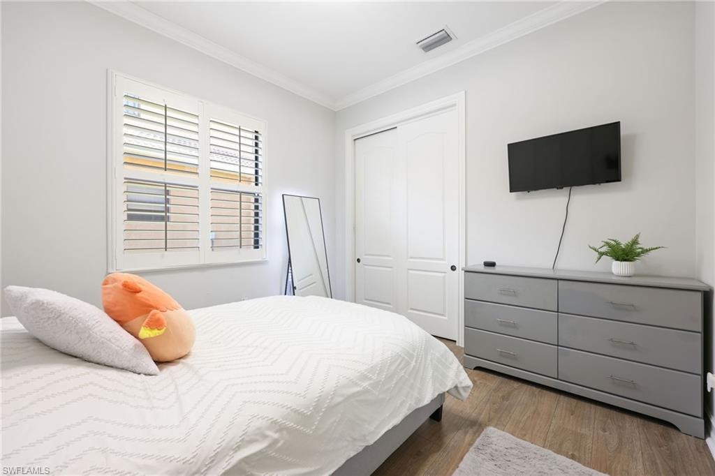 Interior room featuring light gray walls, wood-finish flooring, a white ceiling with crown molding, and a white window with louvered shutters