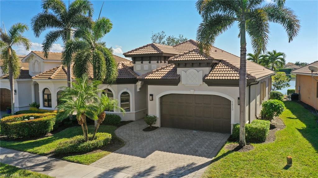 Mediterranean-style residence featuring a tile roof, paver driveway, arched windows, decorative stucco facade, and established tropical landscaping