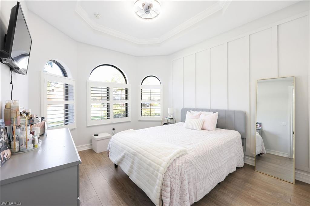 Room featuring wood-finish flooring, a tray ceiling with crown molding, and a decorative ceiling light
