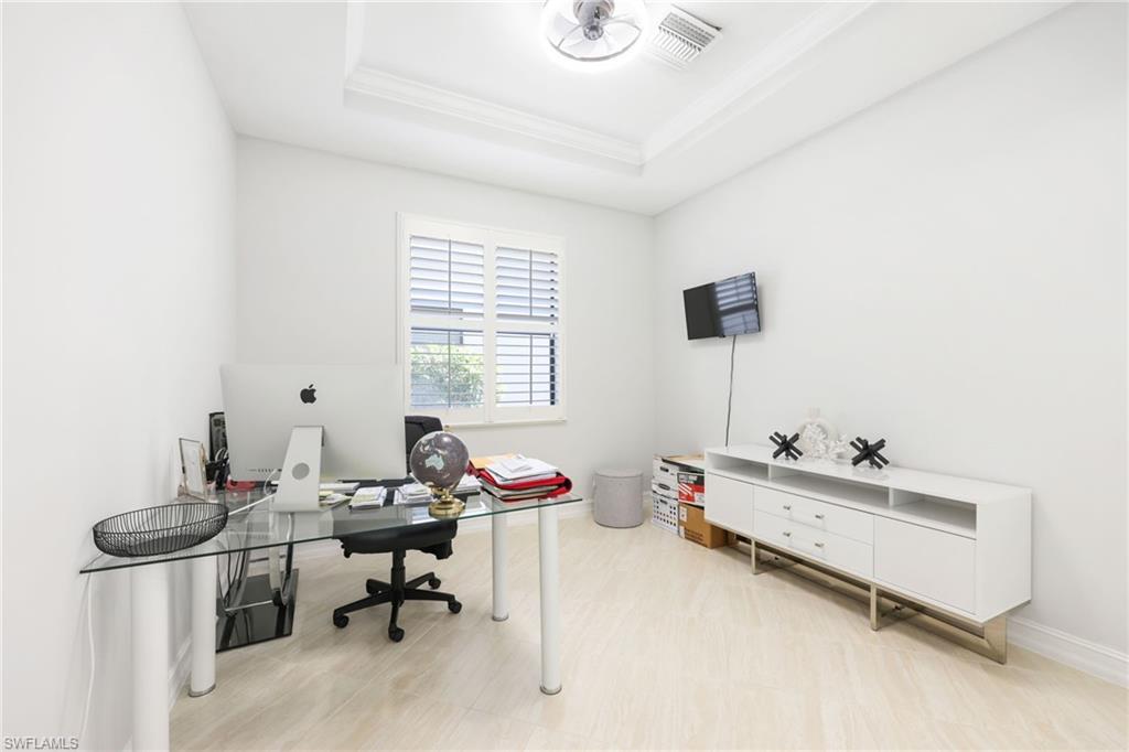 Bright room featuring a window with white louvered shutters, light wood-finish flooring, a tray ceiling, and a built-in wall-mounted television