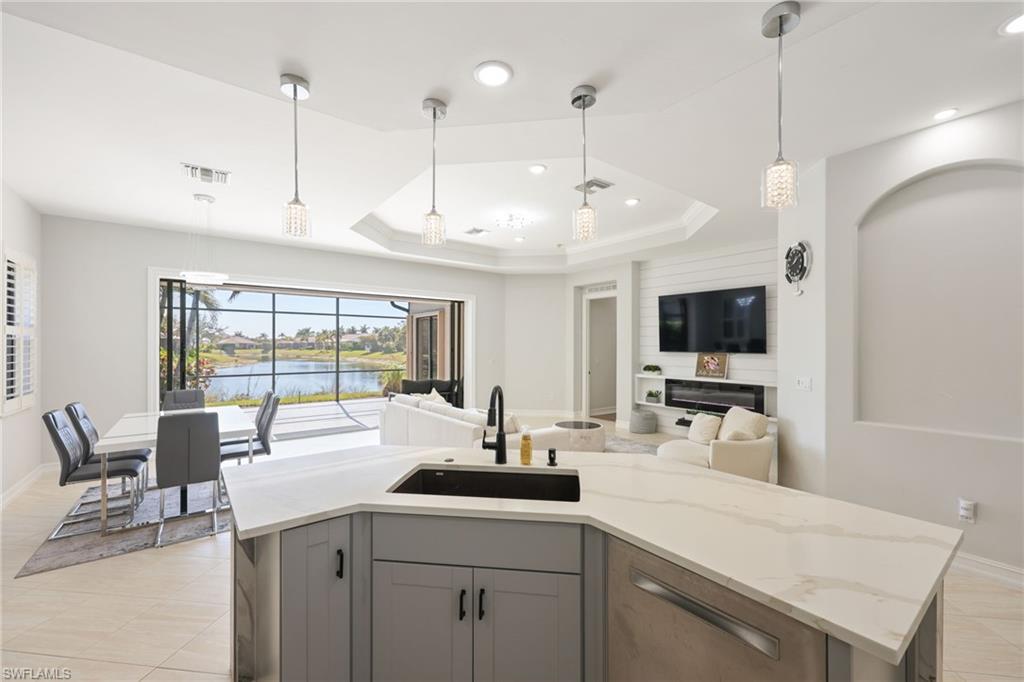Kitchen island with a light-toned countertop, integrated sink, and dishwasher, overlooking a dining area with a rectangular table and an expansive screened lanai