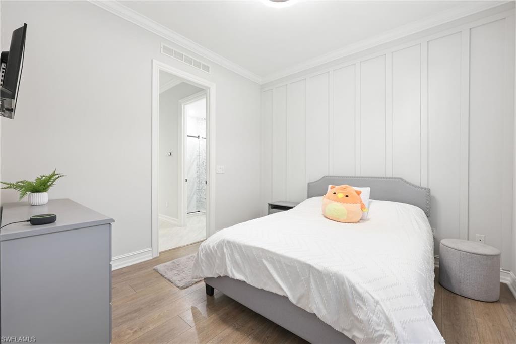 Bedroom featuring wood-finish flooring, crown molding, and a board and batten accent wall