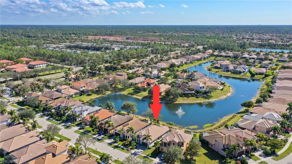 Aerial perspective of a residential community featuring a winding waterway with a fountain, surrounded by properties with tile roofs and mature landscaping