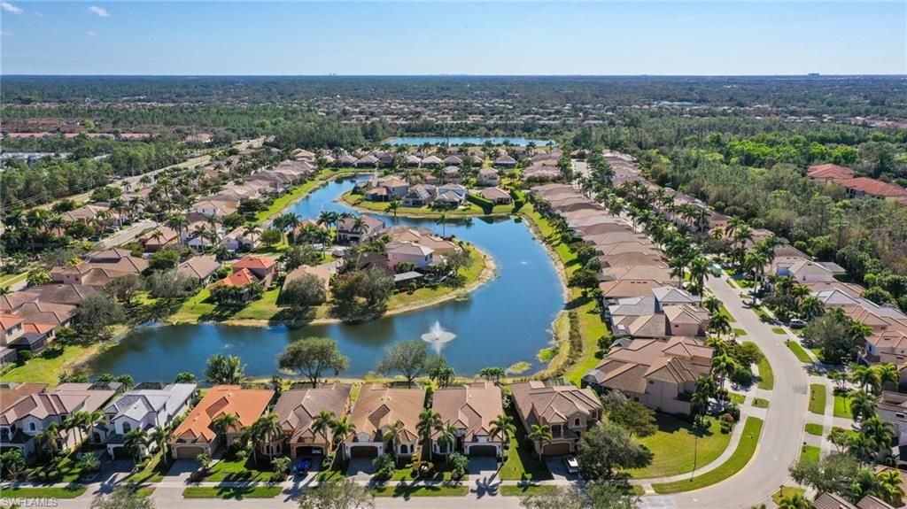 Sprawling residential development featuring a serpentine water feature with a fountain, established landscaping, private roads, and multiple architectural styles under tile roofs
