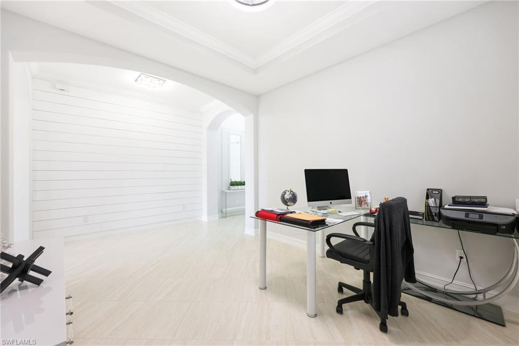 Spacious room featuring light-toned tile flooring, white walls, crown molding, and an arched entryway