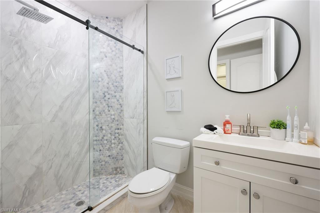 Contemporary bathroom featuring a glass-enclosed shower with a black sliding barn door hardware system, white marble-look tile, and a mosaic pebble floor