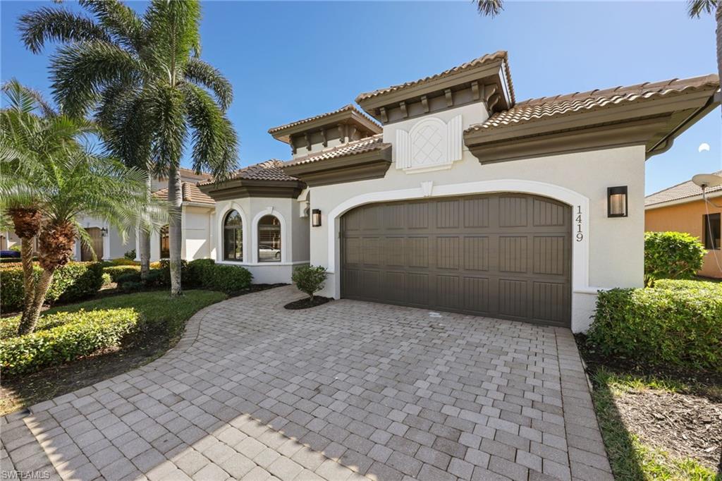 Mediterranean-style exterior featuring stucco finish, barrel tile roof, and a paver driveway