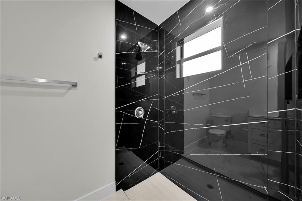 Shower enclosure featuring black polished tile with white veining, glass walls, and a chrome shower head and controls